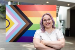 Tessa Dekkers in front of Progress Pride flag; researches digital mental health for LGBTQ+ youth