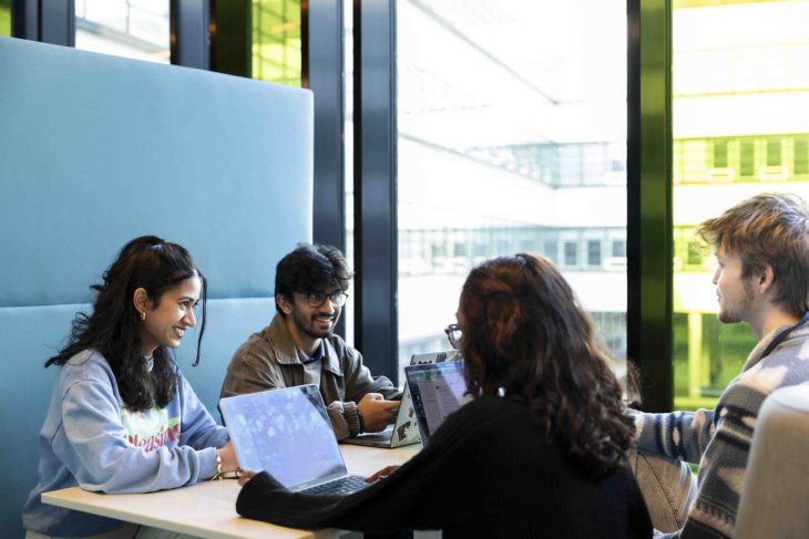 Vier studenten zitten aan tafel te werken aan een gezamenlijk project.