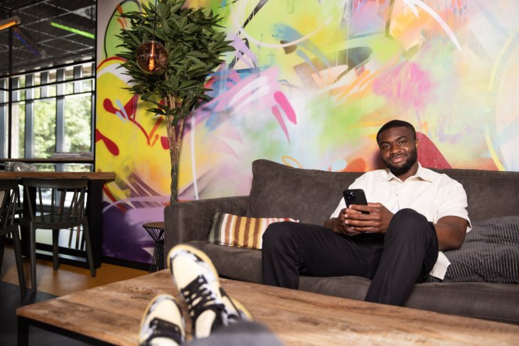 A student sits on a couch with his phone in his hand.