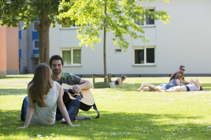 Studenten chillen op het gras en spelen gitaar op de campus
