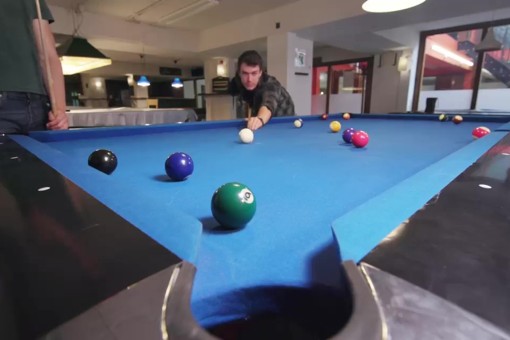 Two students play pool at a pool table to study dynamics in applied physics