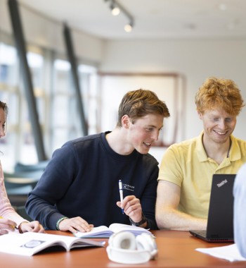 Vier studenten zitten samen aan een tafel te werken aan een project.