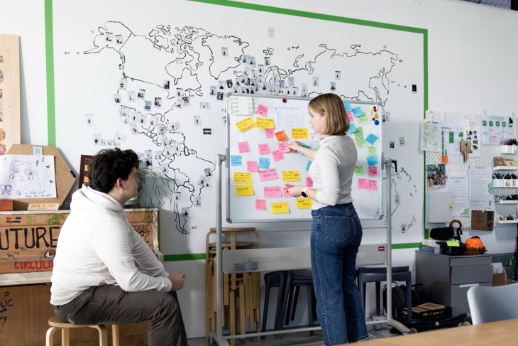 Twee studenten kijken naar een whiteboard vol sticky notes.