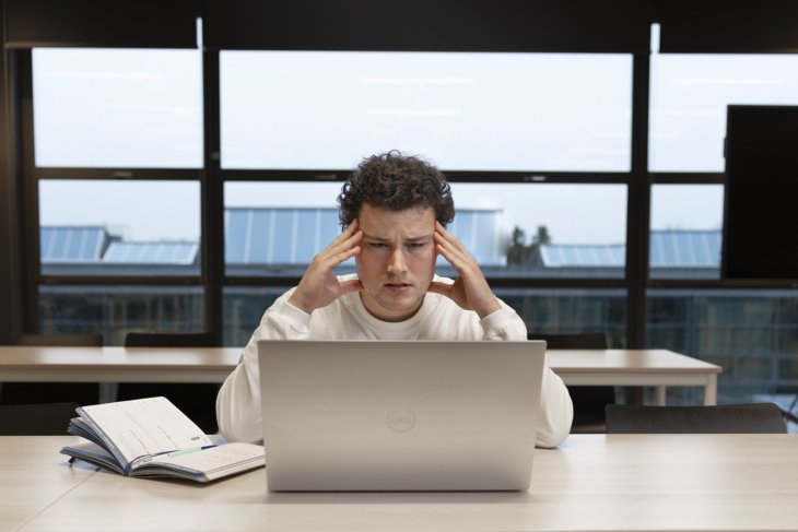 Jongen zit aan tafel en kijkt met een moeilijk gezicht naar zijn laptop
