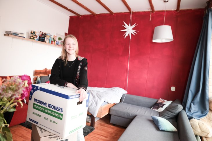 Een student staat in haar kamer met een verhuisdoos.