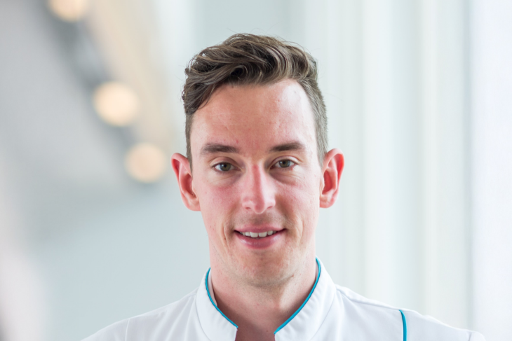 Alumnus Kristian Overduin van de master Technische Geneeskunde lacht in de camera. Hij draagt een doktersjas.