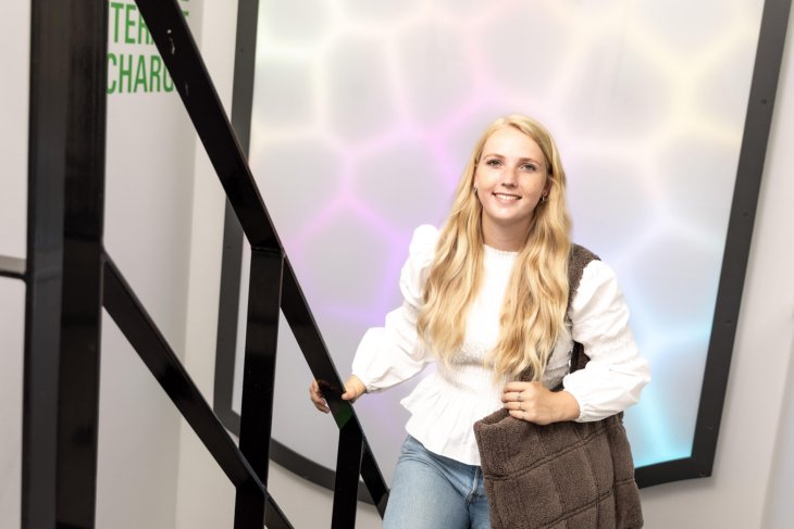 Lachend meisje met witte trui en tas loopt de trap richting de camera