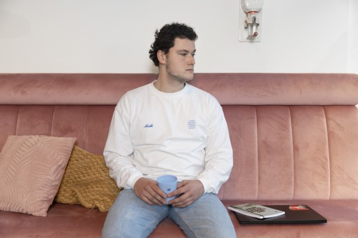 A sad student sits on a couch with his laptop beside him.