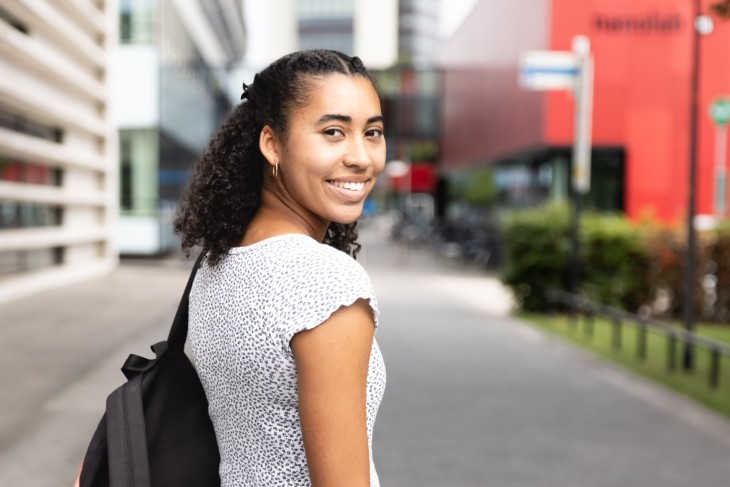 Een student kijkt over haar schouder met een rugzak op.