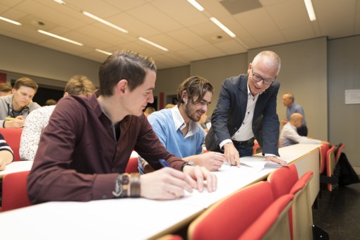 Two students in a lecture hall get help from a professor.