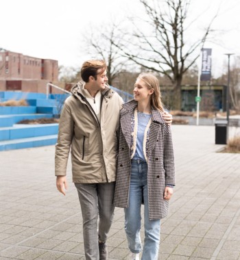 Een studentenkoppel loopt over de campus en lacht naar elkaar.