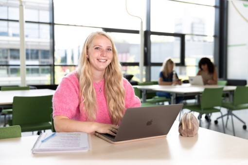 Een leerling zit achter haar laptop te werken en lacht in de camera.