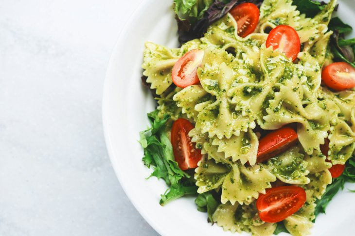 Een bord pasta pesto met tomaten en sla.