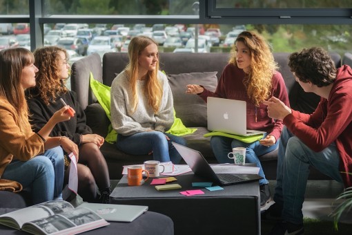 Five students sitting on a couch talking to each other