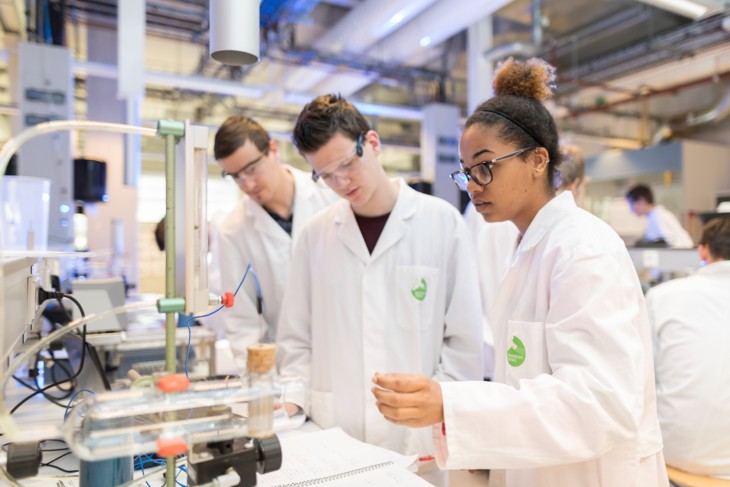 Three students at work in a laboratory, wearing white lab coats