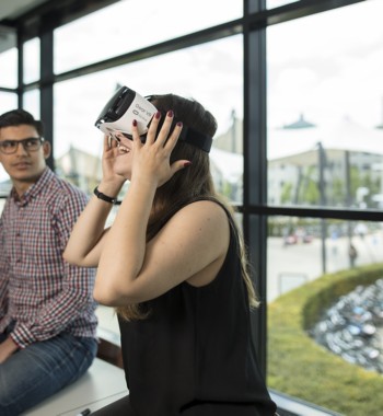 Een student zit in de vensterbank te kijken naar een andere student die een VR bril draagt.