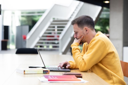 A student sits behind his laptop to study.
