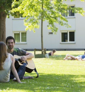 Studenten chillen op het gras en spelen gitaar op de campus