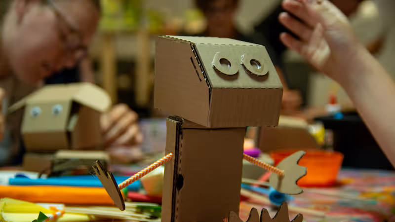 A toy puppet made of cardboard sits on a table surrounded by children