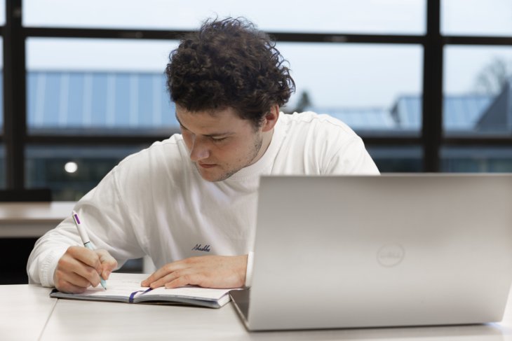 A student working on his thesis behind his laptop.