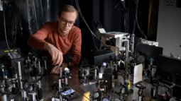 A student adjusts a photonics setup with lenses, mirrors, and optical components.