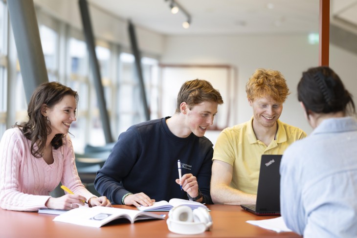 Vier studenten zitten samen aan een tafel te werken aan een project.