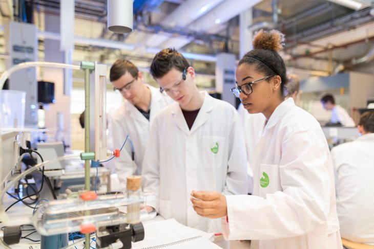 Drie studenten aan het werk in een laboratorium, met witte laboratoriumjassen aan