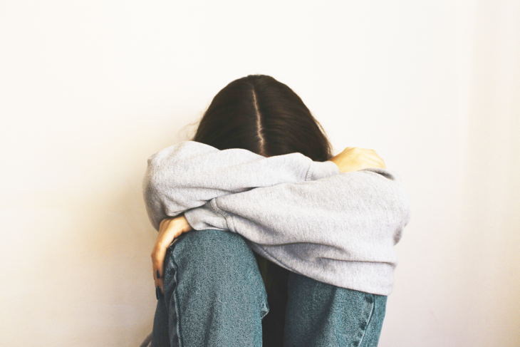 A student sits on the floor with her head in her arms.