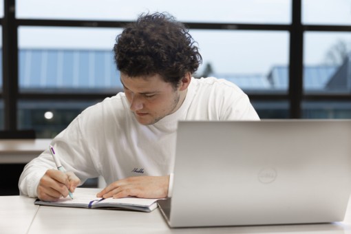 A student working on his thesis behind his laptop.