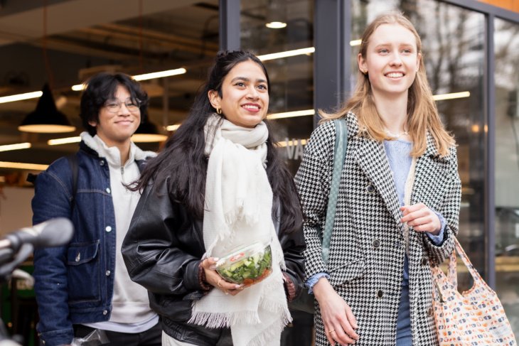 Three students come out of the campus supermarket with groceries.