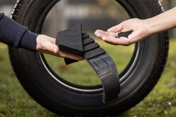 Sustainable rubber research: hands holding rubber granulate and components in front of a car tire.