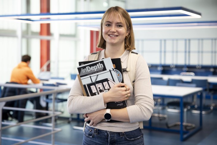 Een student van de Universiteit Twente houdt een stapel boeken in haar handen en lacht naar de camera.