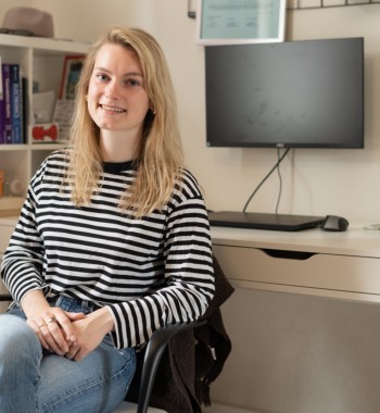 Een student zit op haar thuiswerkplek en lacht in de camera.