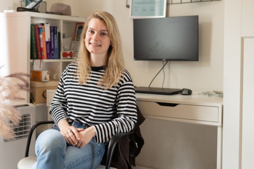 A student sits at her home office and smiles into the camera.