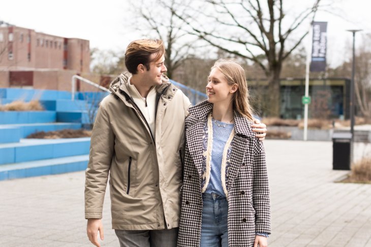 Een studentenkoppel loopt over de campus en lacht naar elkaar.