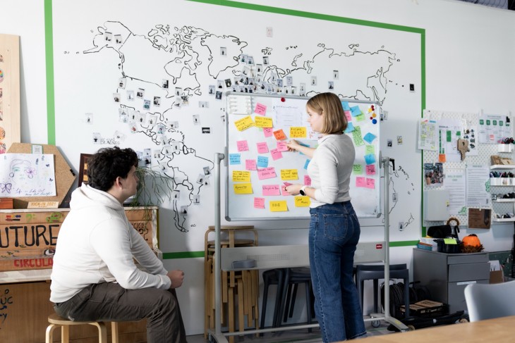 Two students looking at a whiteboard full of sticky notes.