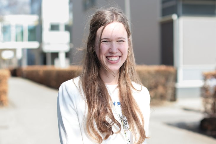 Student Jasmijn buiten op de campus, lachend in de camera.