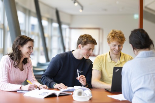 Vier studenten zitten samen aan een tafel te werken aan een project.