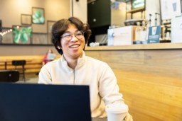 Student Wisang zit achter zijn laptop en lacht naar iemand achter de camera.